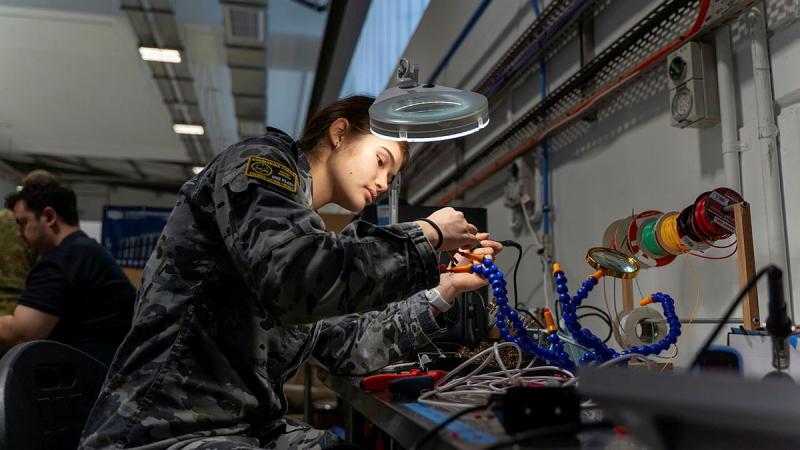 A woman in Navy uniform works on soldering a robot.