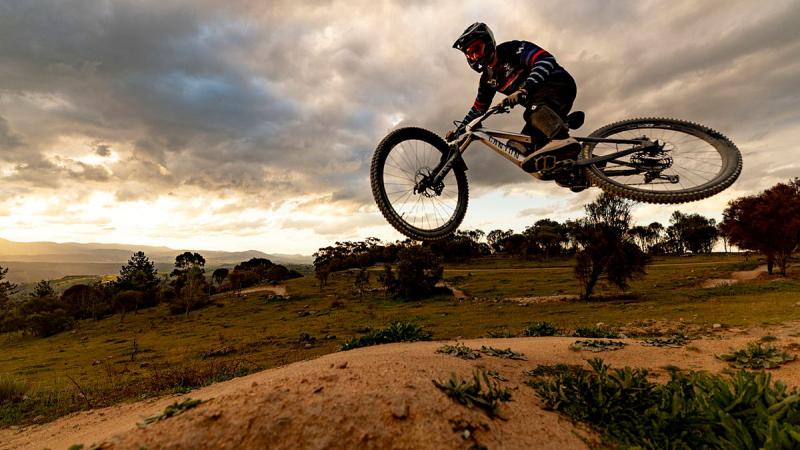Cyclist hovers mid-air above the sandy and grassy ground