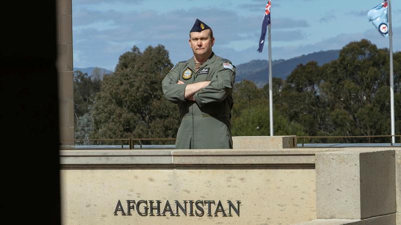 A military man stands with his arms crossed in front of a concrete block with the word 'Afghanistan' on it.