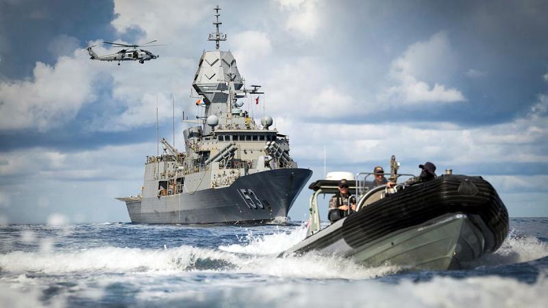 A small boat drives away from a large ship and helicopter at sea.
