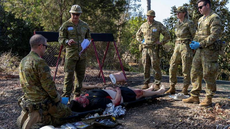 A group of Army people stand around a person lying on the ground with burns makeup.