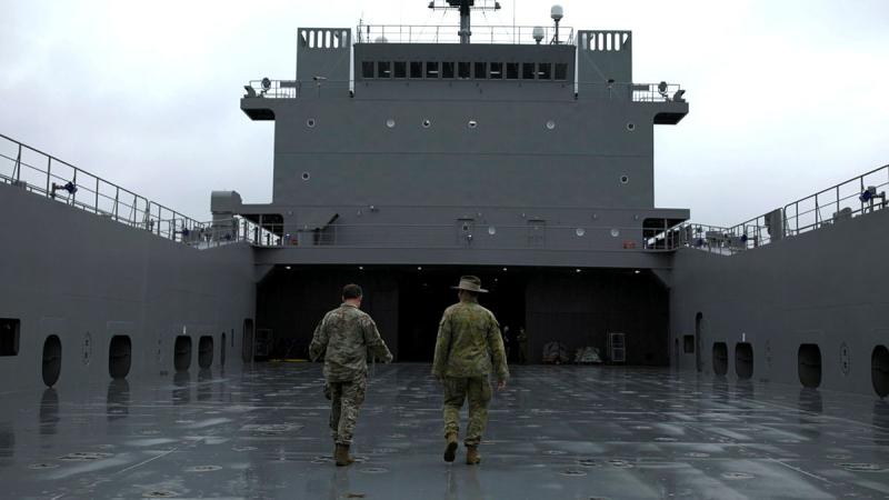Two uniformed people walk down the deck of a large ship.