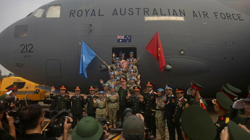 Vietnamese and Australian Air Force personnel stand in front of a Royal Australian Air Force plane waving flags at a media scrum.