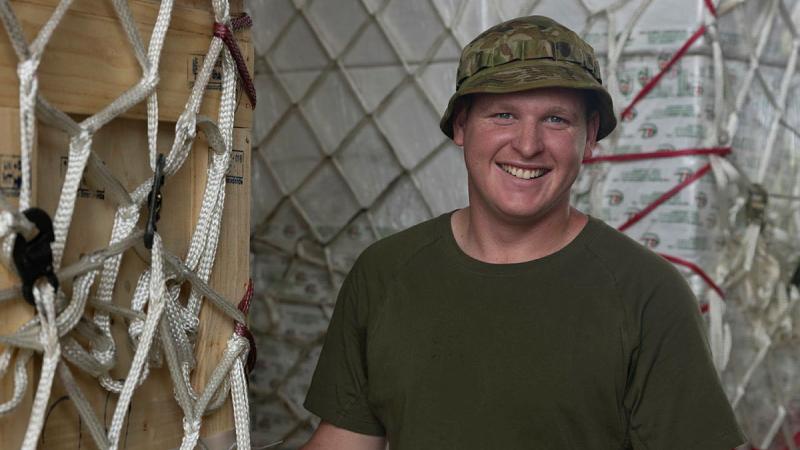 A military man smiles next to boxes covered in netting.