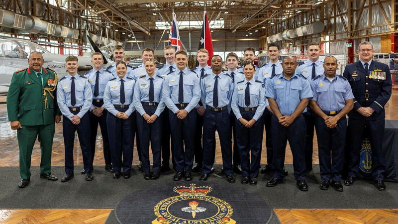 A large group of military personnel in a warehouse-like place, with two national flags.