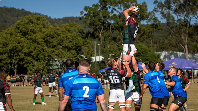 Men playing rugby on a field lift a teammate into the air while he holds a rugby ball above his head.