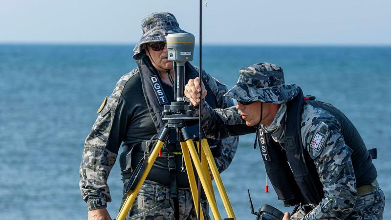 Two Navy members set up weather equipment on the beach.
