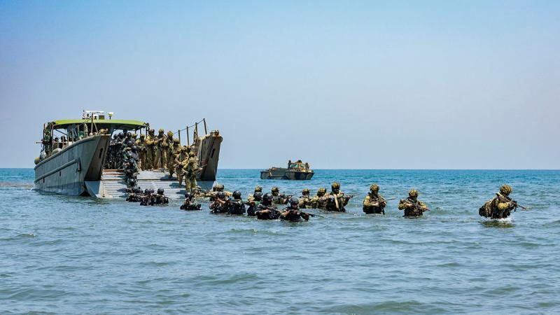 Armed soldiers pile out of a military ship and through chest-high water.
