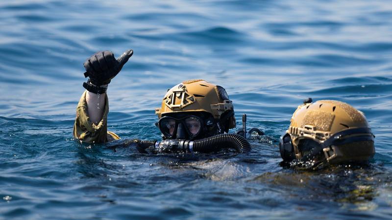 Two divers heads seen poking above the surface of the ocean, with one giving the thumbs up signal.