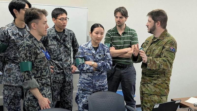 A group of military members and a civilian engage in discussion in an office area.