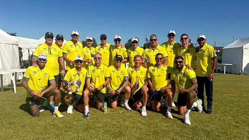 A group of men in matching yellow and green uniform stand or kneel together on grass.