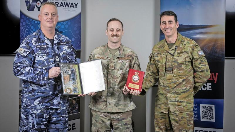 Three military men stand with two awards between them.