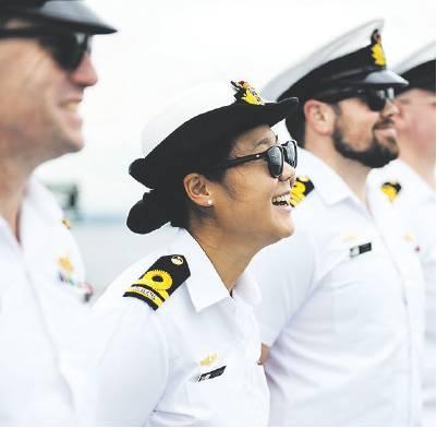 Several people wearing white naval uniforms and peaked caps stand in a row outdoors. The person in the foreground is wearing dark sunglasses and a white uniform with rank insignia on the shoulders. Other uniformed personnel are visible in the background, slightly out of focus.