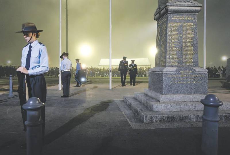 Military personnel leaning on rifles surround a memorial at dusk.