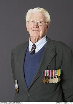 Formal portrait of an older adult standing against a dark gray background.