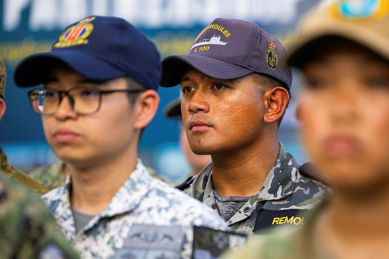 An Australian Navy member stands with international military partners.
