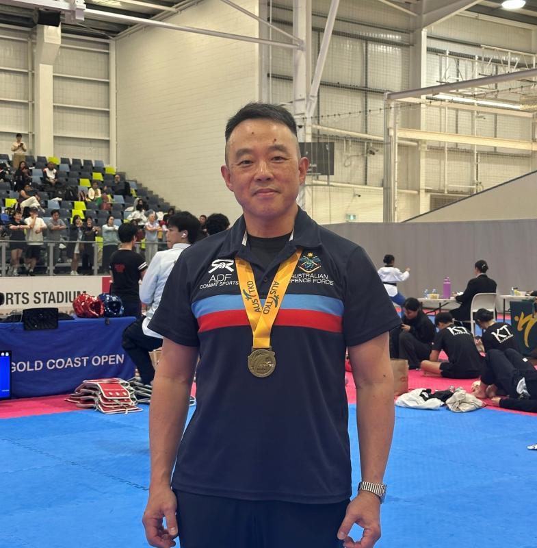 Man stands in a gymnasium with a gold medal hanging from his neck