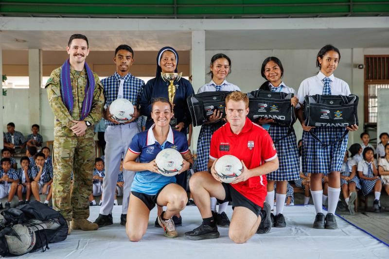 A group of students, civilians and military personnel with soccer equipment.