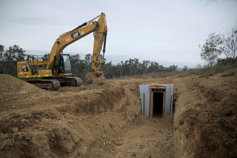 A yellow digger is positioned near a dug out area, complete with an entryway made from metal and wood.
