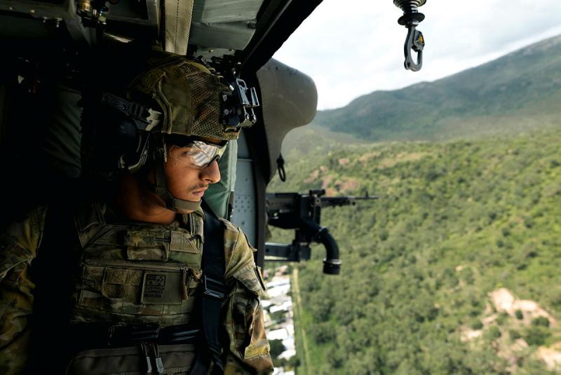 A soldier looks out from a helicopter to bushland. 