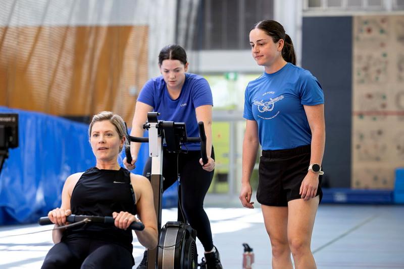 One woman on a rowing machine, one women on an exercise bike and another woman keeping watch.