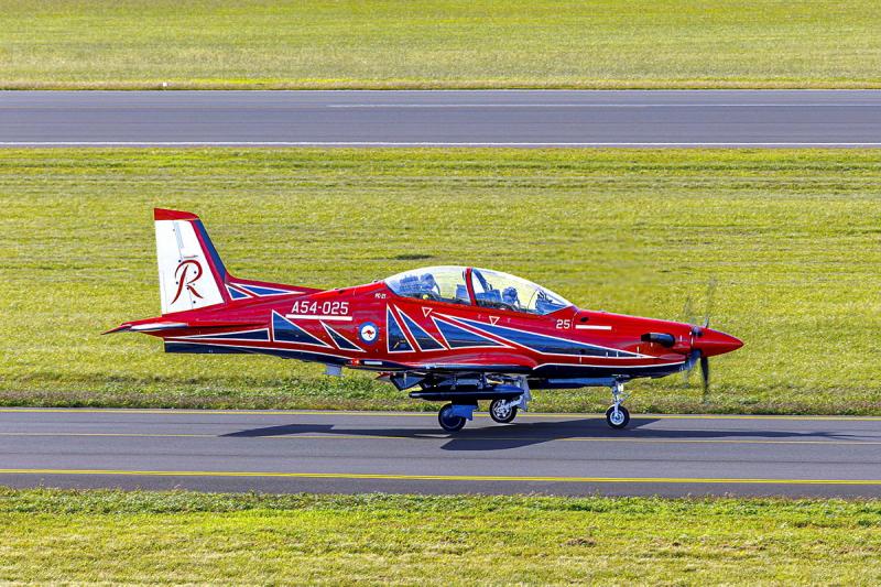A red aircraft on the runway preparing to take off.