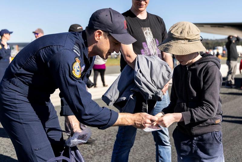 Roulette Five, Flight Lieutenant David Burnard, gives a Canberra local child stickers at the Canberra Airport Open Day 2026.
