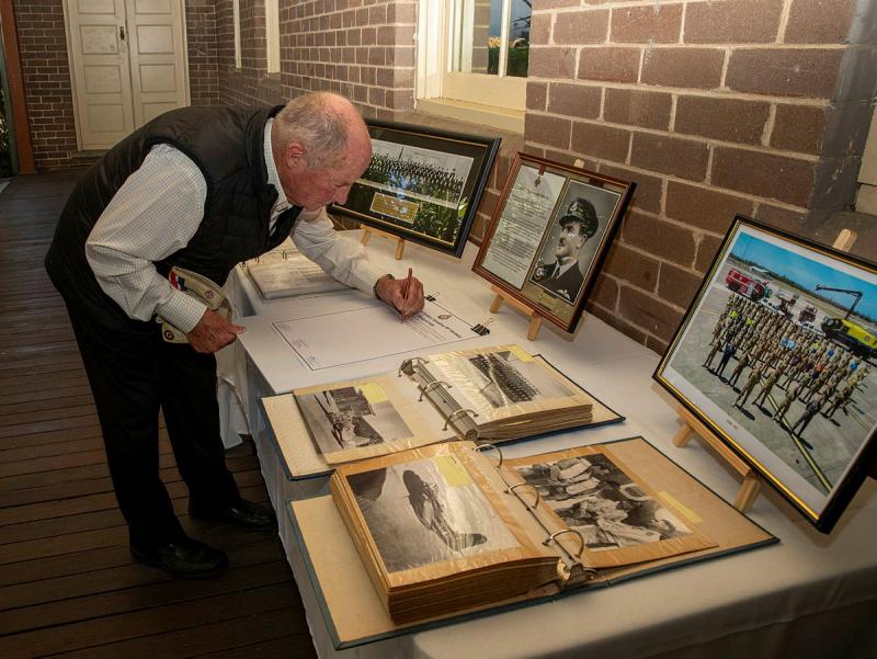 A older man writing in a book on a table.