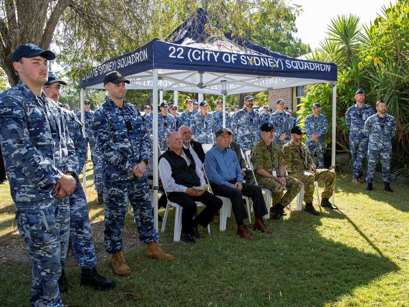 Air Force personnel standing around a gazebo, which people sitting on chair underneath it.