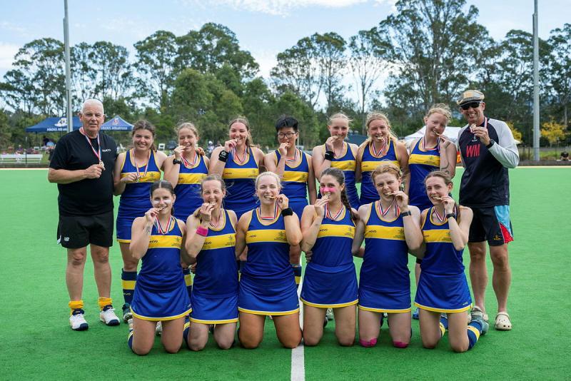 A group of women in sports uniform pose for a photo, biting on their medals.