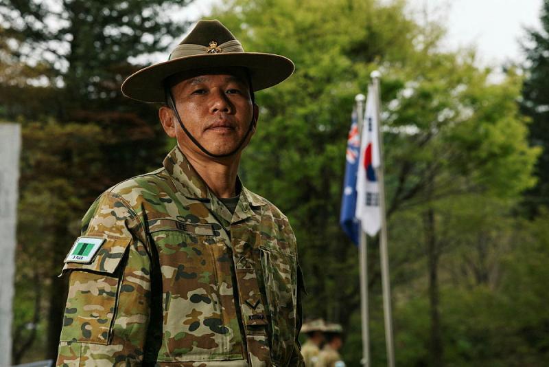 A military man stands outside before two flags.