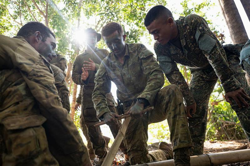 Military personnel try to start a fire outdoors.