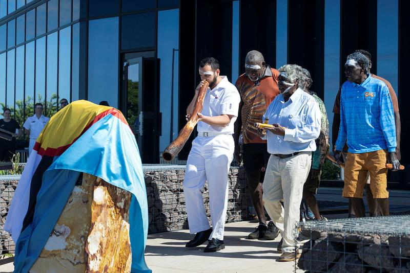 A group of people walking along, with one playing the didgeridoo.