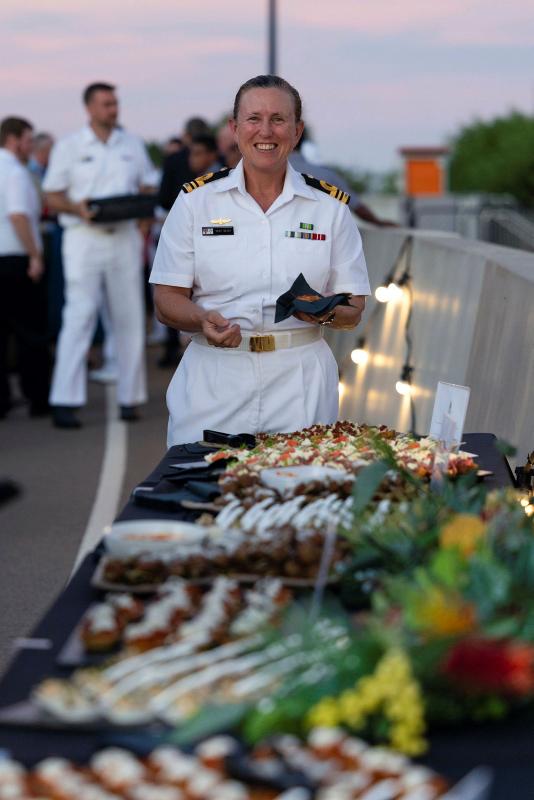 A Navy member stands, smiling, at the end of a table full of food.