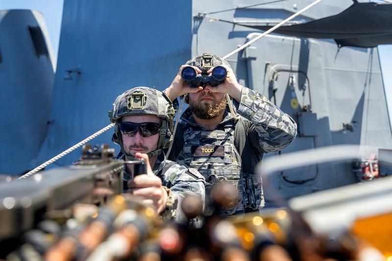 One sailor fires a machine gun as another looks out with binoculars. 