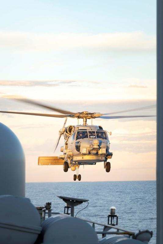 A helicopter flies near the deck of a ship at sea.