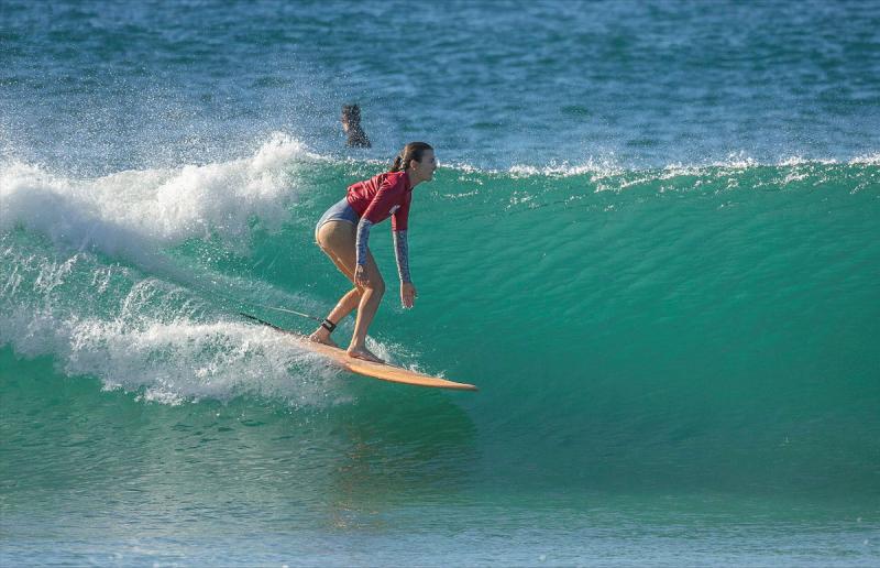 A female surfer rides an aqua blue wave.