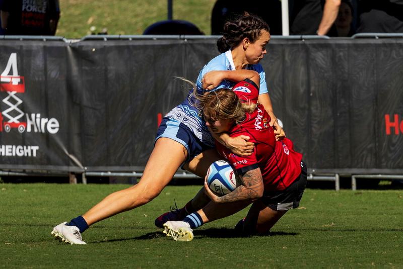 A female rugby player tackles another female rugby player during a game.