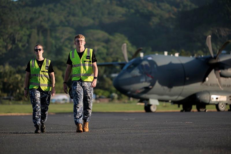 Two military members walk away from an aircraft in the mountains.