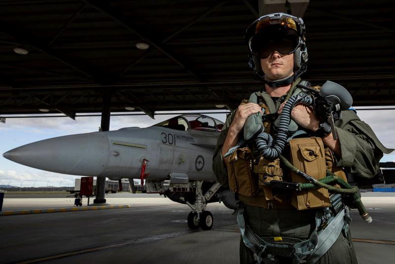 An aviator in full kit stands next to an aircraft in a hangar.