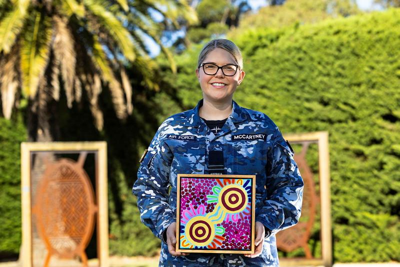 A woman in Air Force uniform holding up an Aboriginal artwork.