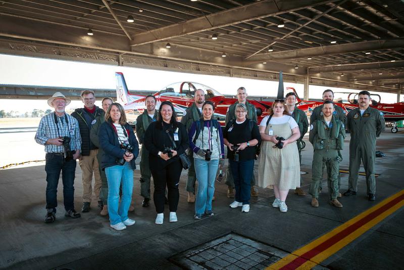 Civilians and pilots stand in front of an aircraft in a hangar.