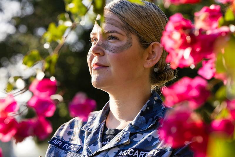 A woman with face paint standing amongst pink flowers.