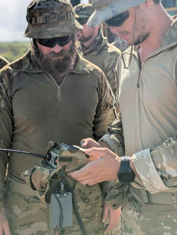 Two military personnel use a device with an antenna.