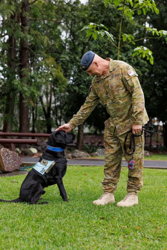 A military member interacts with a service dog outside.