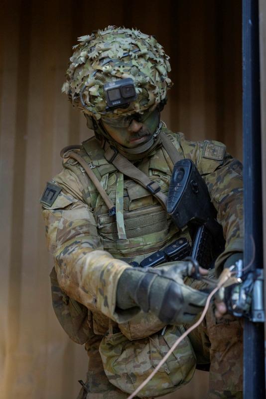 A soldier tends to the wires on a simulated device on a door of a building.