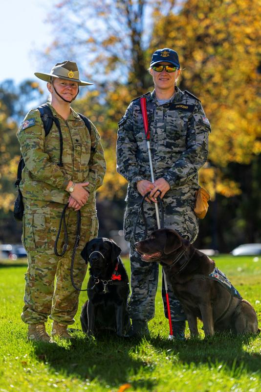 Two women in uniform with two black dogs.