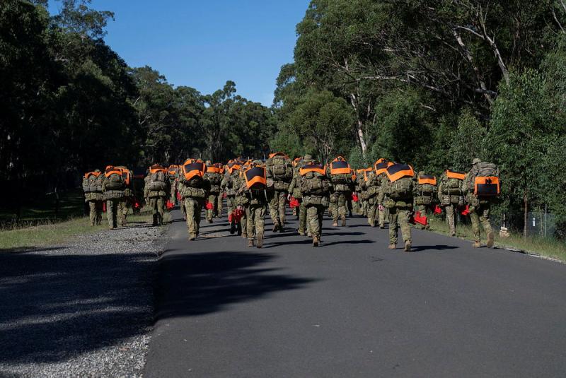 A large group or people in Army uniform pack marching along a road.