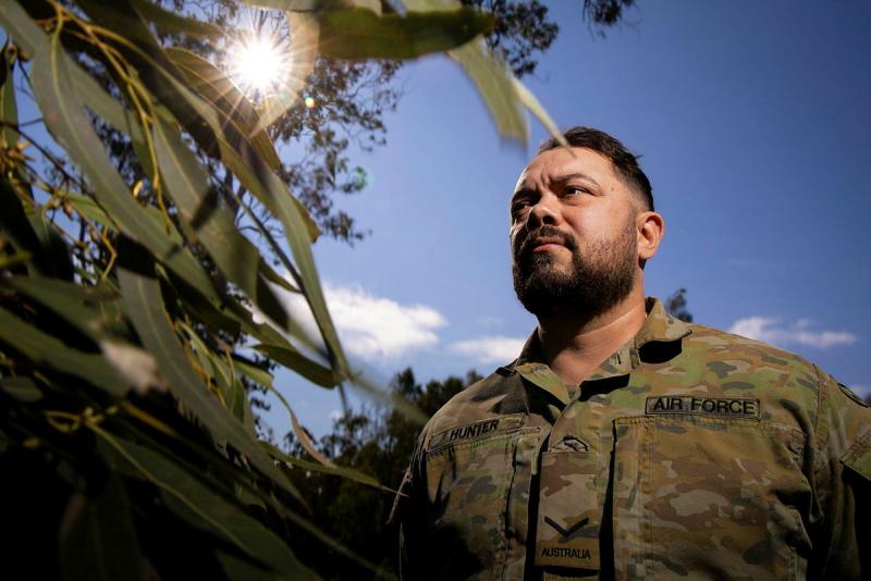 A military man standing by a eucalyptus tree stares into the distance.