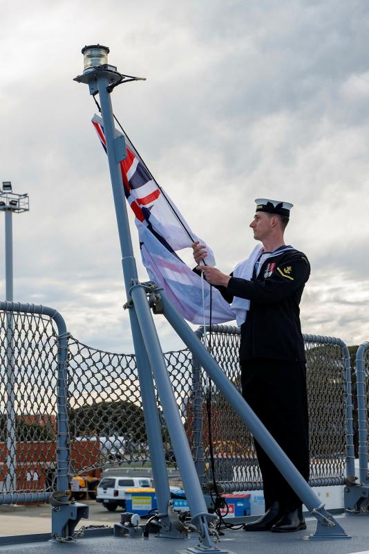 A sailor stands next to a flagpole, holding a flag attached to it.